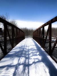 Footbridge in snow covered bridge against sky