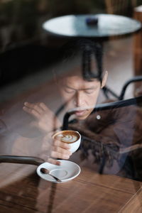 Man having coffee seen through glass window