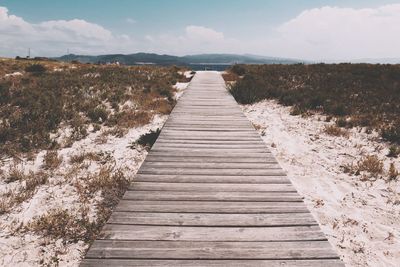 Boardwalk leading towards pier against sky