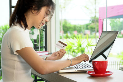 Young woman holding credit card while using laptop at home
