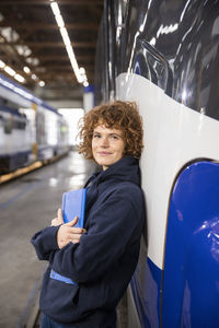 Smiling engineer holding file folder leaning on monorail at industry