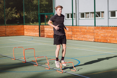 Blond boy in sportswear jumps over red obstacles to improve lower body dynamics