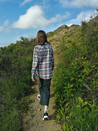 Girl in checkered shirt going forward on the mountain path against the sky