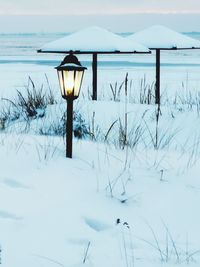 Illuminated street light on snow covered field against sky