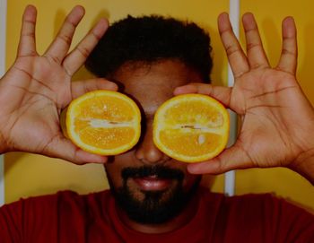 Close-up man holding covering eyes with oranges at home