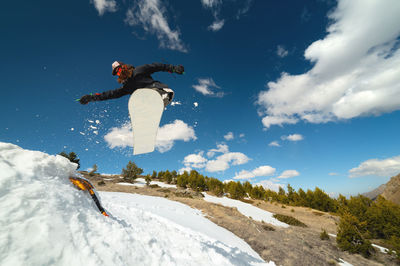 Snowboarder woman jumping from a kicker springboard from the snow on a sunny day in the mountains