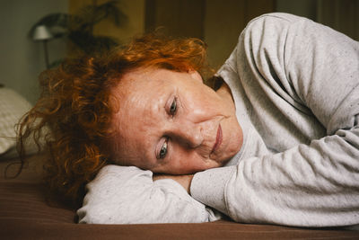 Sad senior woman contemplating while lying on bed at home