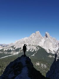 Rear view of woman standing on mountain against clear blue sky