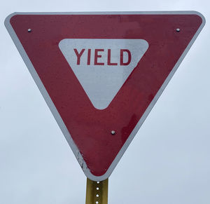 A red and white yield sign close up with white sky background.