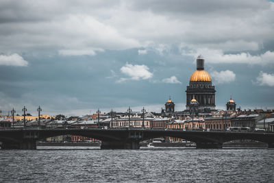 Bridge over river in city against cloudy sky