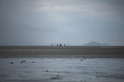 Surface level view of people walking on shore at beach against sky