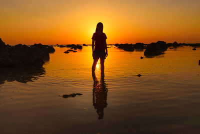 Silhouette woman wading in sea against sky during sunset