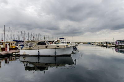 Sailboats moored at harbor against cloudy sky