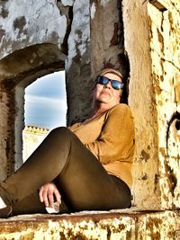 Woman wearing sunglasses sitting on wall