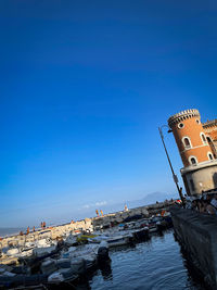 Buildings by sea against clear blue sky