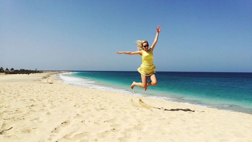 Woman jumping on beach against clear blue sky