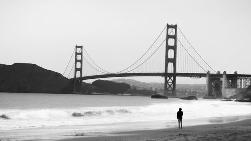 Rear view of silhouette person standing at beach against golden gate bridge