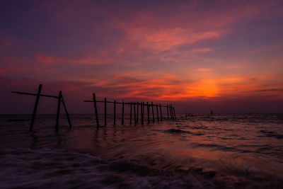 Wooden posts on beach against sky during sunset