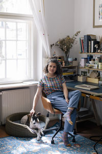 Woman stroking dog while sitting on chair at home