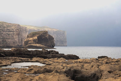 Rock formation on beach against sky