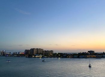 Sea by buildings against clear sky during sunset