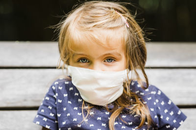 Portrait of cute girl wearing flu mask sitting outdoors