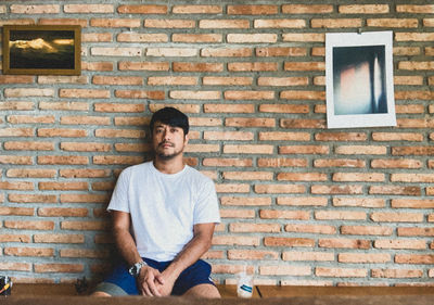 Portrait of a smiling young man sitting against brick wall