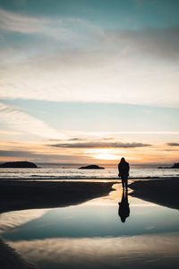 Silhouette man standing on beach against sky during sunset