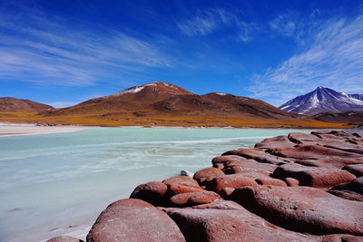 Scenic view of sea by mountains against blue sky