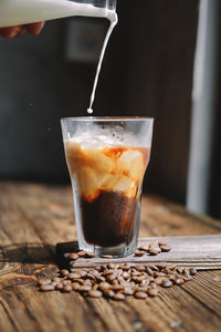 Cropped hand pouring milk in iced coffee on wooden table
