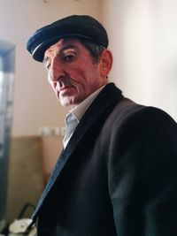 Portrait of senior man wearing hat standing against wall at home