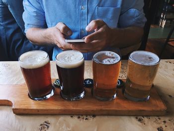 Midsection of man using phone while standing by beer glasses on tray