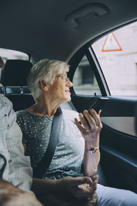 Elderly woman holding smart phone while sitting in car during vacation