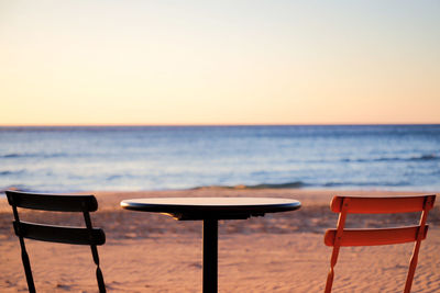 Empty chairs and table by sea against sky