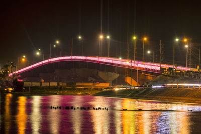 Illuminated bridge over river against sky in city at night