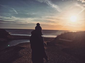 Woman standing at beach against sky during sunset