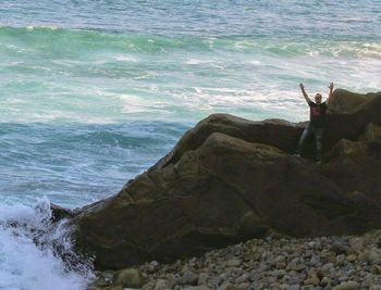 Man standing on rock at sea shore against sky