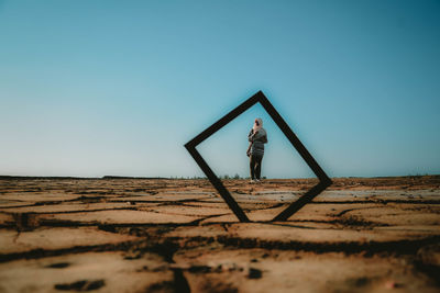 Woman seen through picture frame on land against clear blue sky