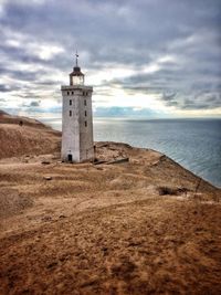 Lighthouse on beach against cloudy sky