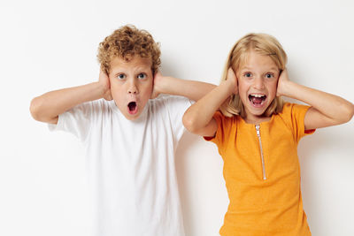 Portrait of sibling covering ears against white background