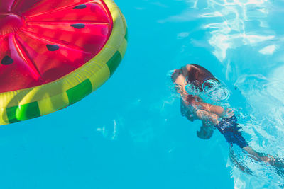 Boy swimming in pool with watermelon float