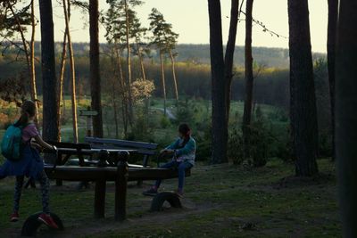 Rear view of couple sitting on bench in forest