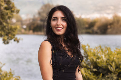 Portrait of smiling young woman standing against lake