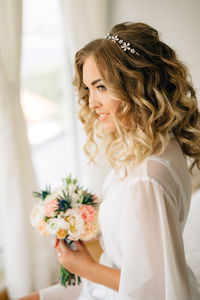 Smiling bride holding bouquet at home