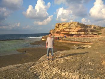 Rear view of man standing on rock by sea against sky