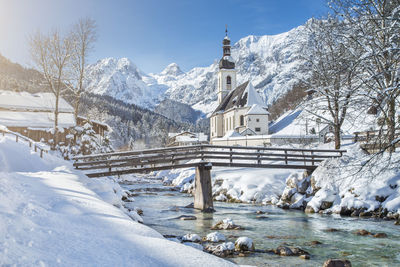 Snow covered church by river against sky