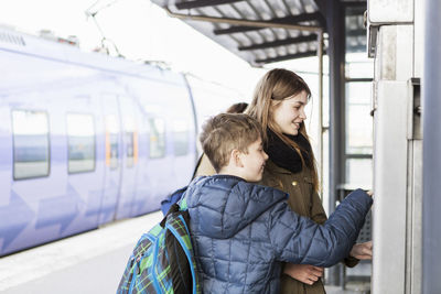 Siblings buying tickets from automated machine at train station