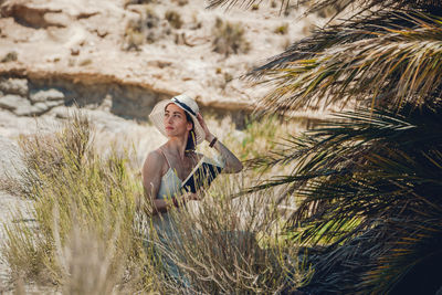 Woman wearing hat holding book while sitting against mountain