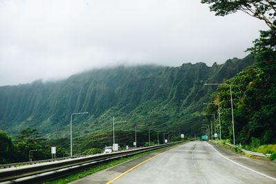 Empty road leading towards mountains against clear sky