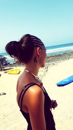 Side view of young woman standing on beach against clear sky